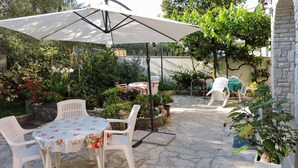 A patio area with a table and chairs, surrounded by potted plants and a large umbrella. - Nice apartment in Peroj with swimming pool (Peroj)