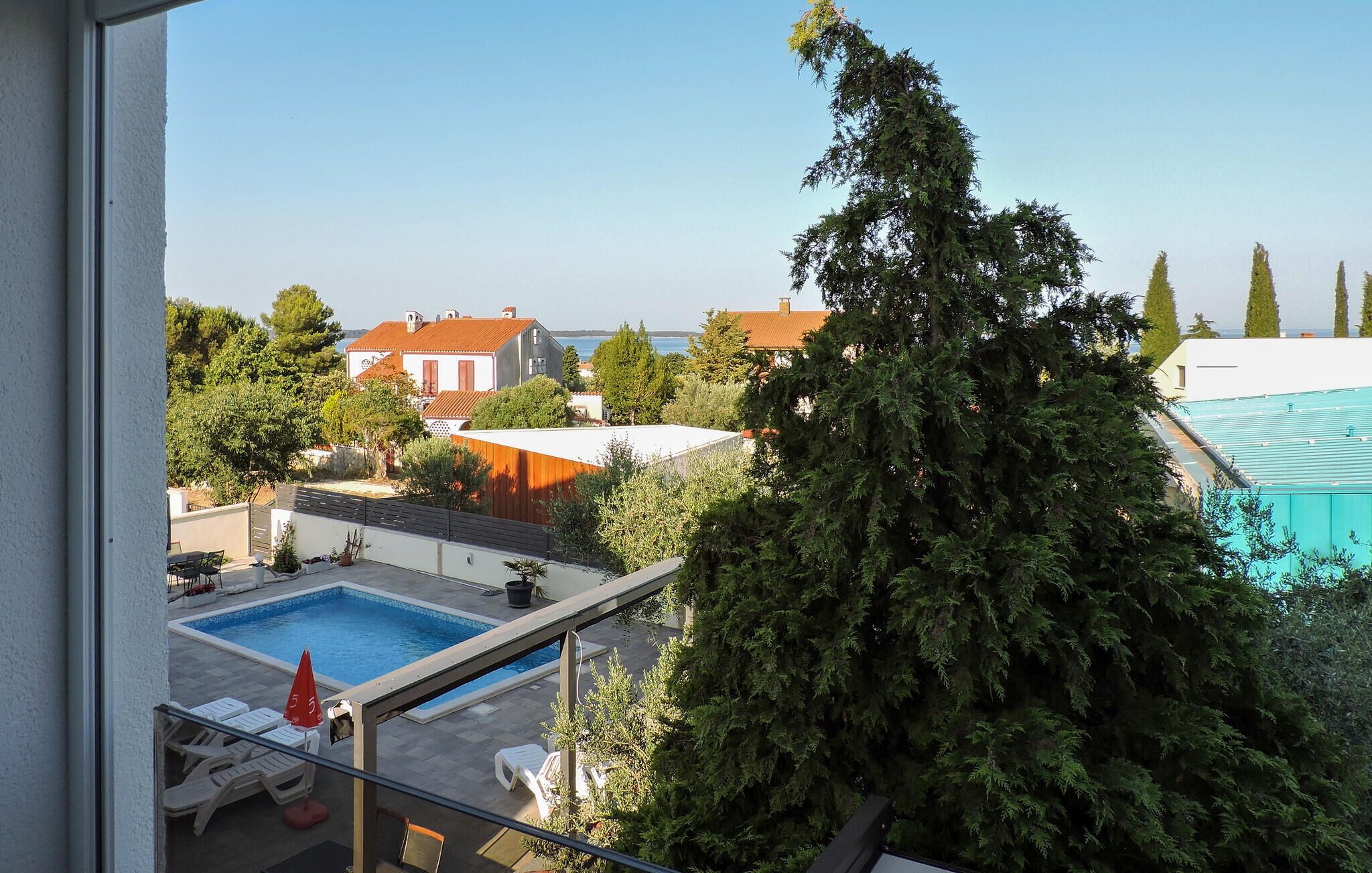 A residential area with a swimming pool, a large tree, and houses with red roofs.