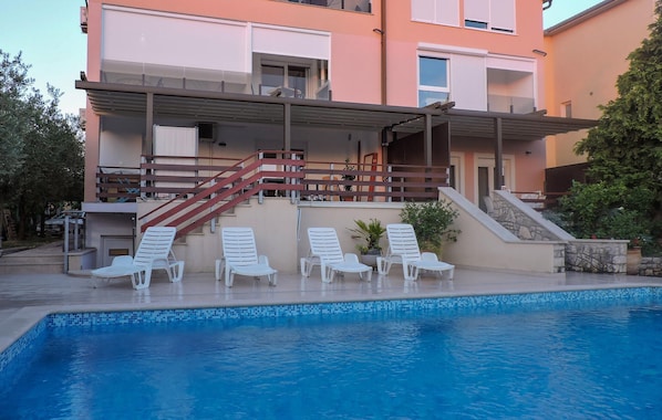 Ein modernes Gebäude mit Pool, weißen Liegestühlen und einer Treppe, die zu einem Balkon führt.