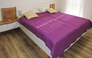 Ein Bett mit violettem Überwurf, einem Holz-Kopfteil und zwei Nachttischen mit Lampen.