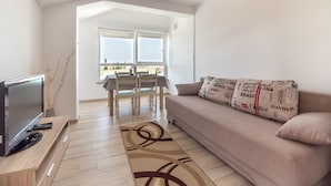Ein modernes Wohnzimmer mit Flachbildfernseher, Holzmöbeln, einem beigefarbenen Sofa und einem gemusterten Teppich.