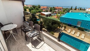 Ein Balkon mit Tisch und Stühlen, der einen Blick auf ein Schwimmbecken und das Meer bietet.