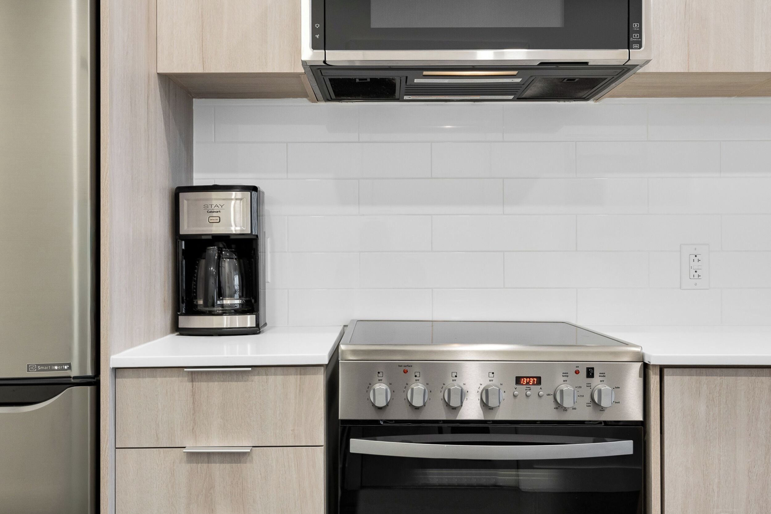Una cocina con estufa de acero inoxidable, cafetera y microondas encima.