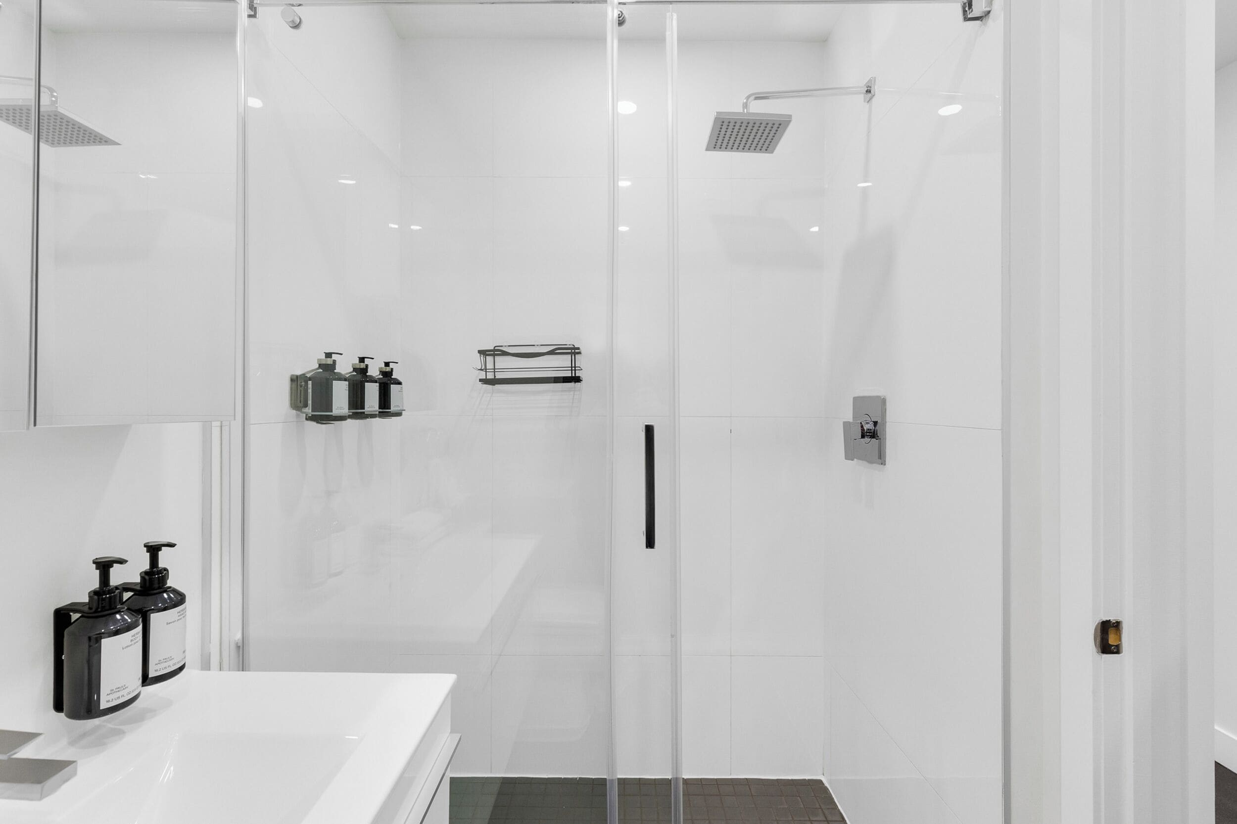 A modern bathroom with a glass shower enclosure, a white sink, and two soap dispensers.