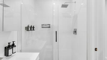 A modern bathroom with a glass shower enclosure, a white sink, and two soap dispensers.