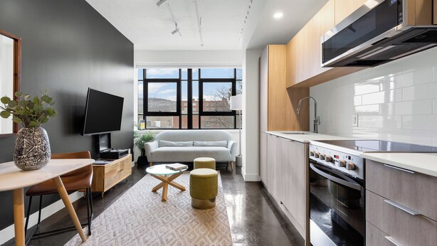 A modern kitchen with a built-in oven, a dining area with a table and chairs, and a sofa in the living area. - The Cove Hotel (Montréal)