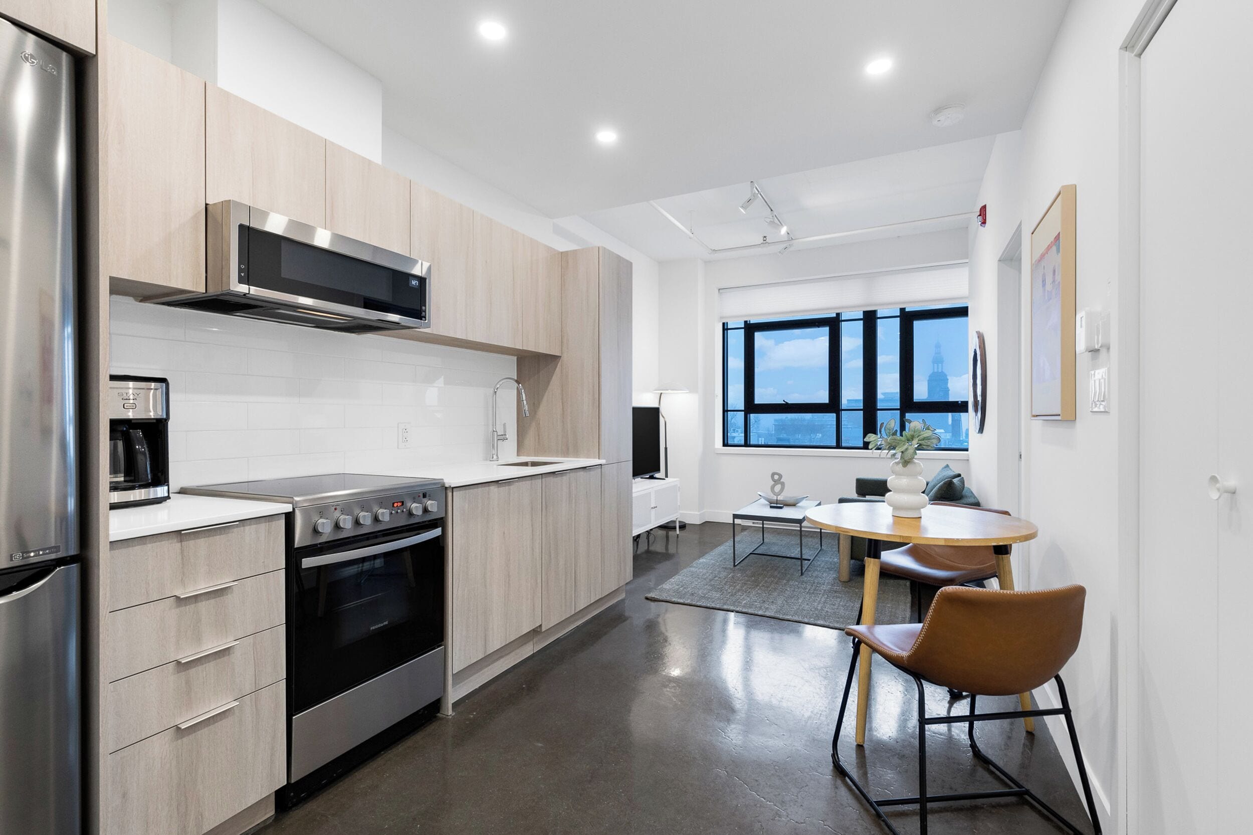 Een moderne keuken met roestvrijstalen apparatuur, houten kastjes en een eethoek met een tafel en stoelen.