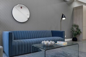 Un salon moderne avec un canapé bleu, un miroir rond, une lampe sur pied et une table basse en verre.