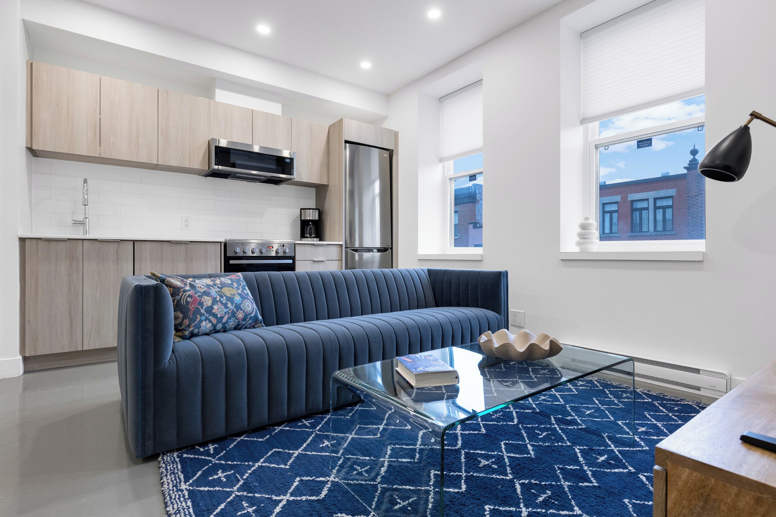 Ein modernes Wohnzimmer mit einem blauen Sofa, einem Glastisch und einem blau gemusterten Teppich.