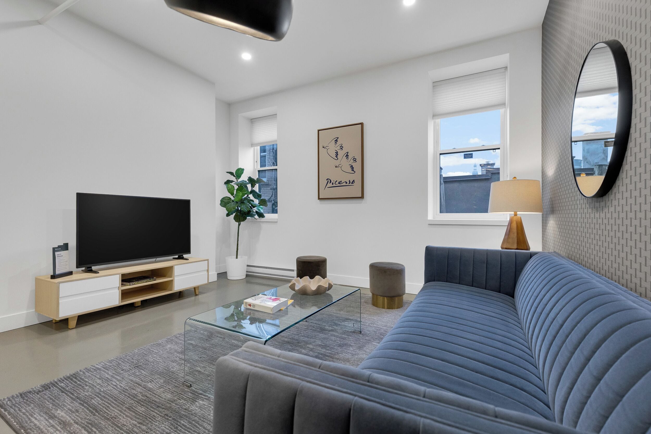 Een moderne woonkamer met een flatscreen televisie, een glazen salontafel, een blauwe bank en een kunstwerk in een lijst aan de muur.