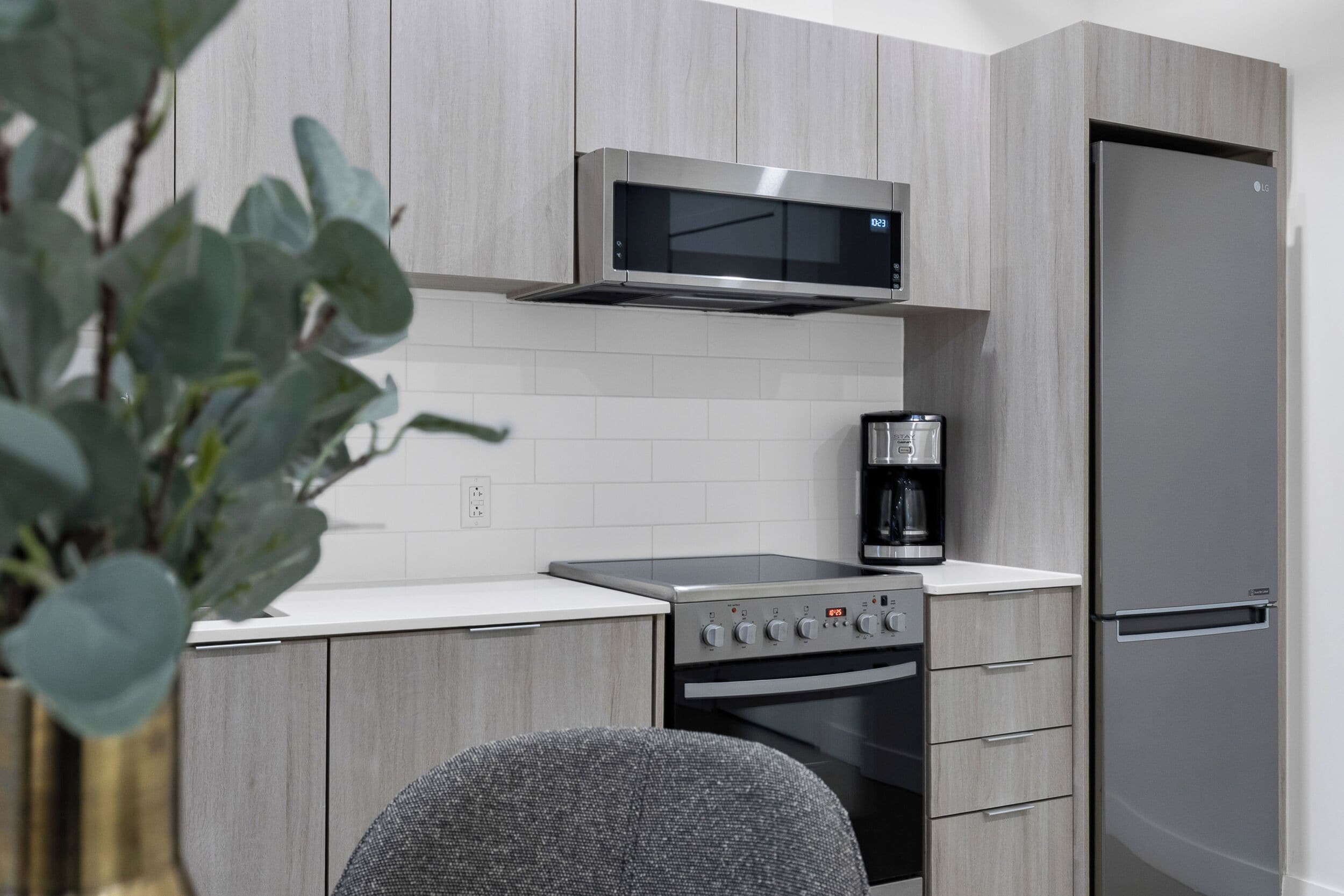 Una cocina moderna con armarios grises, un microondas de acero inoxidable, una cafetera y un refrigerador.