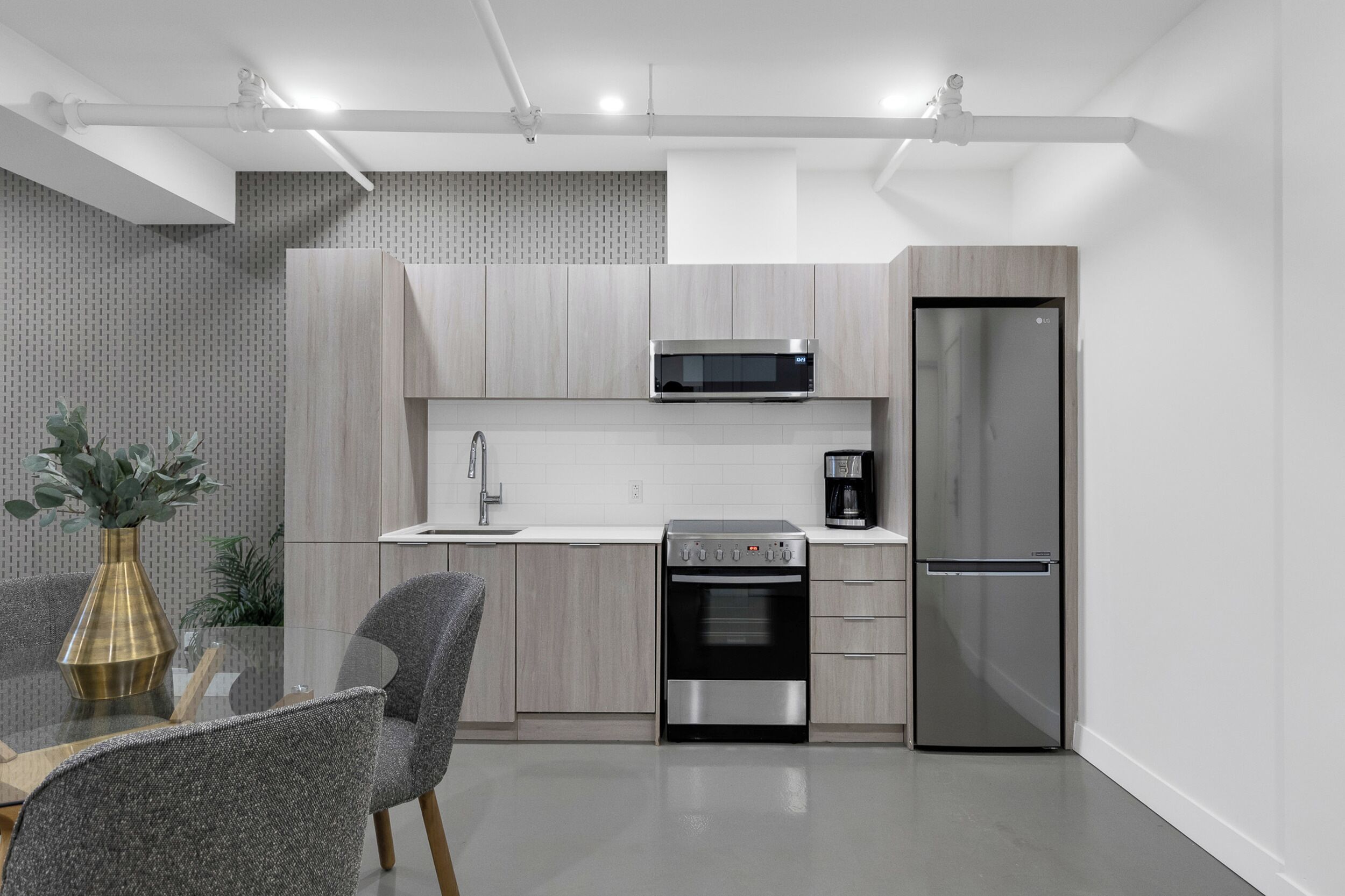 Una cocina moderna con armarios de madera clara, electrodomésticos de acero inoxidable y una mesa de comedor de vidrio con sillas.