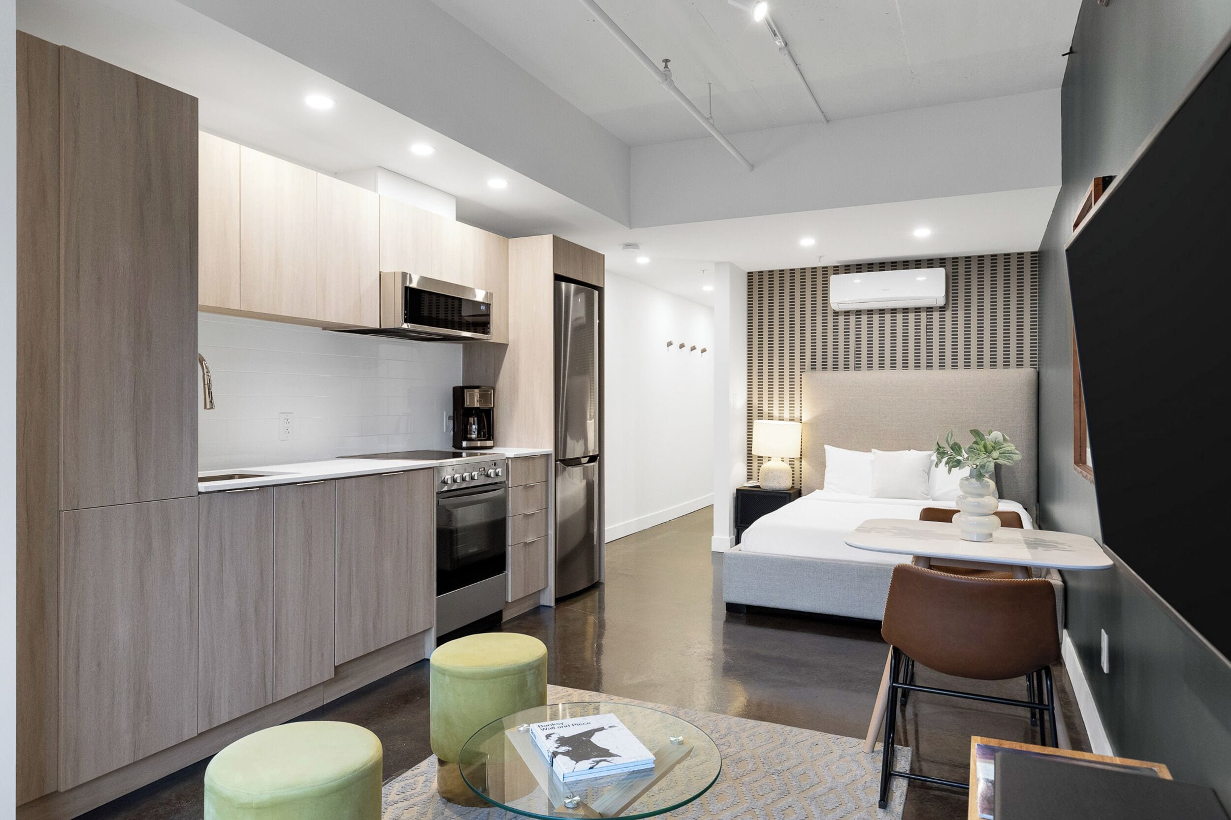 Een moderne keuken met roestvrijstalen apparatuur, een eethoek met een glazen tafel en een slaapkamer met een bed en nachtkastje.