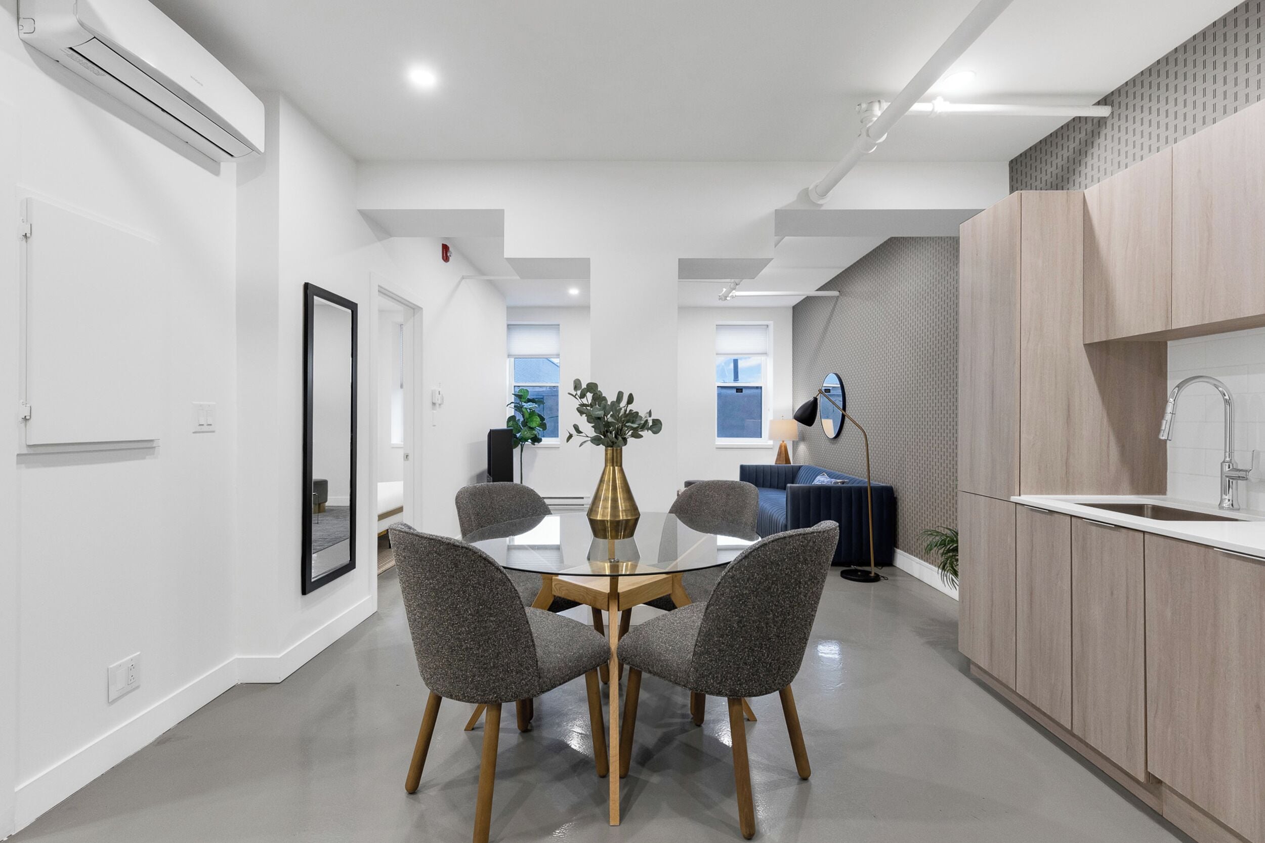 A modern kitchen with a central island, a dining area with a glass table, and a view of the outside.