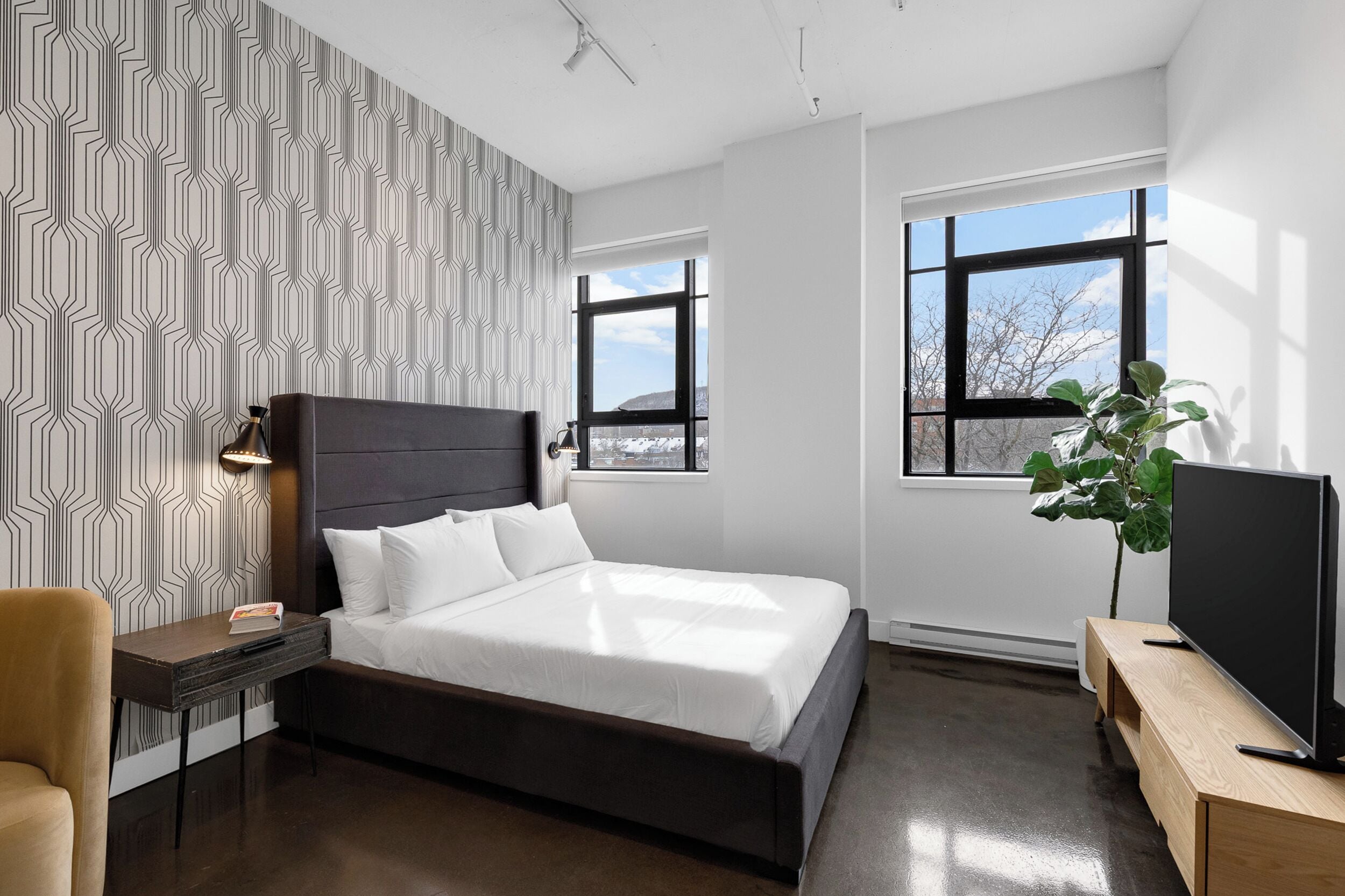 A modern bedroom with a large bed, a TV, and a window with a view of trees.