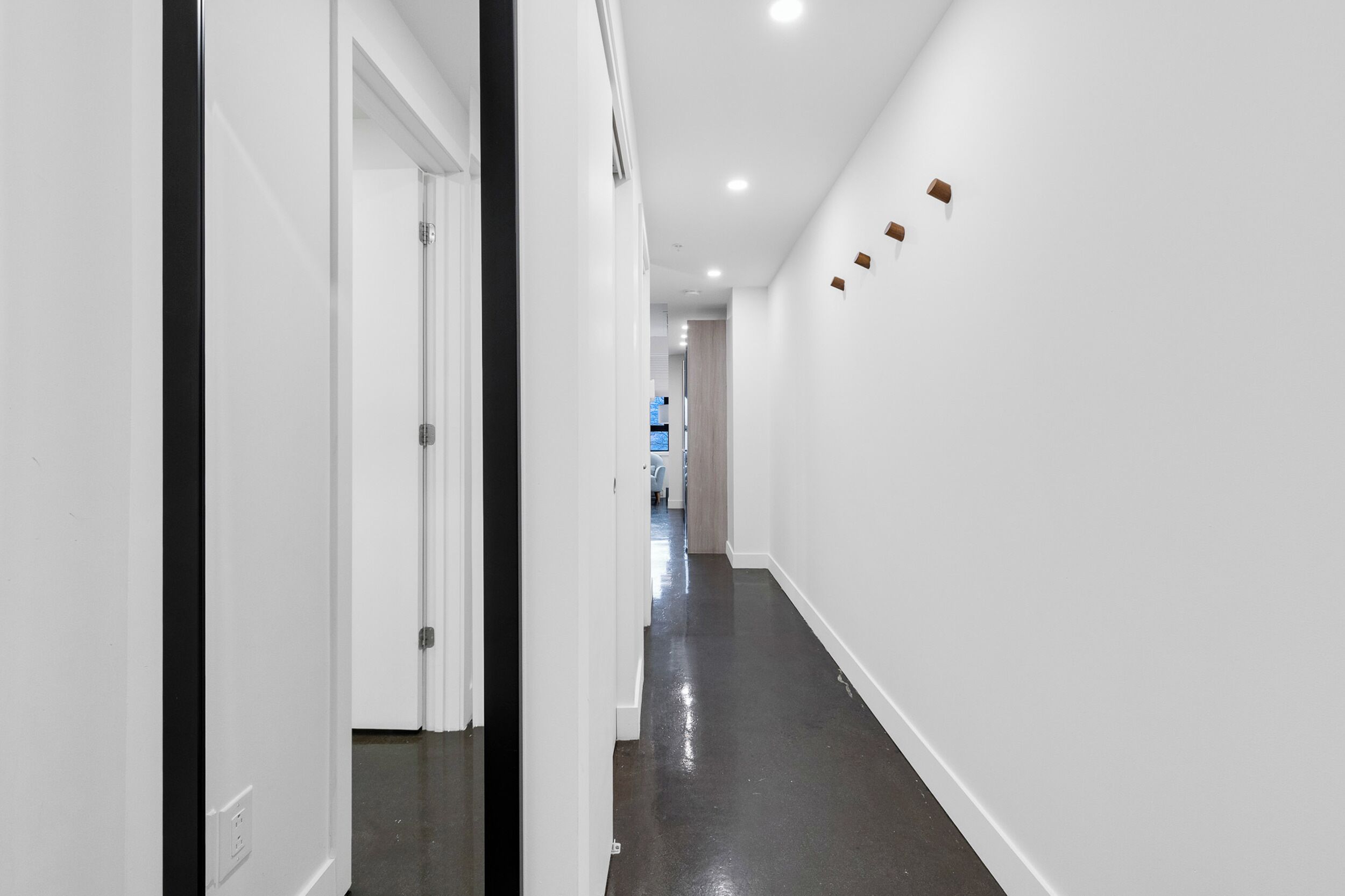 Un pasillo con paredes blancas, piso oscuro e iluminación empotrada.