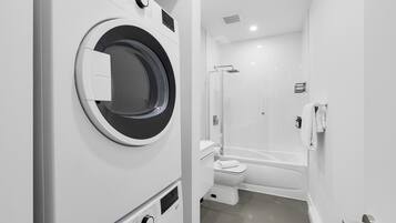 A compact, modern bathroom with a built-in washing machine, a toilet, and a bathtub.