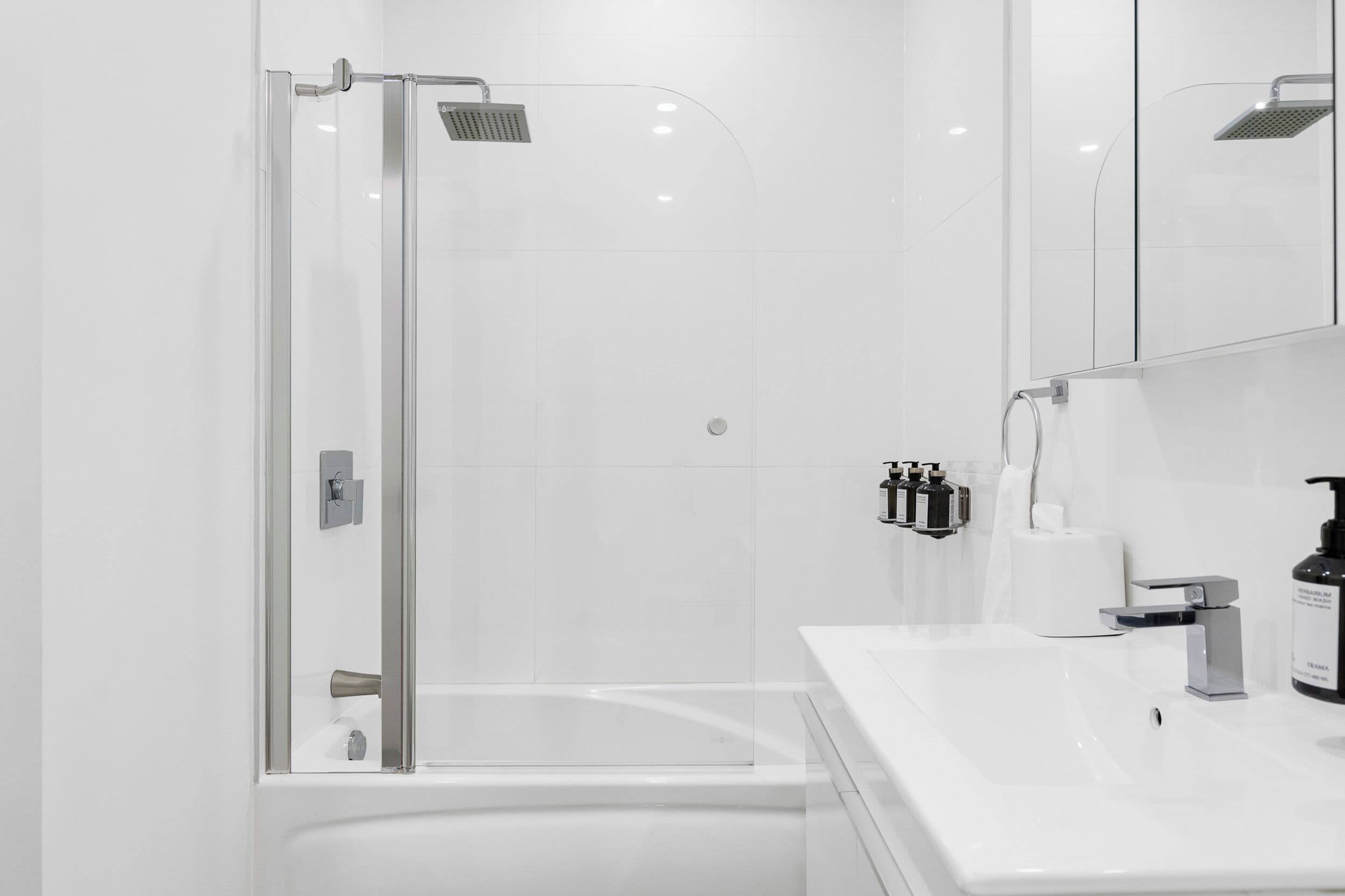 Un baño moderno con ducha compartimentada por vidrio, un lavamanos blanco y un espejo sobre el lavamanos.