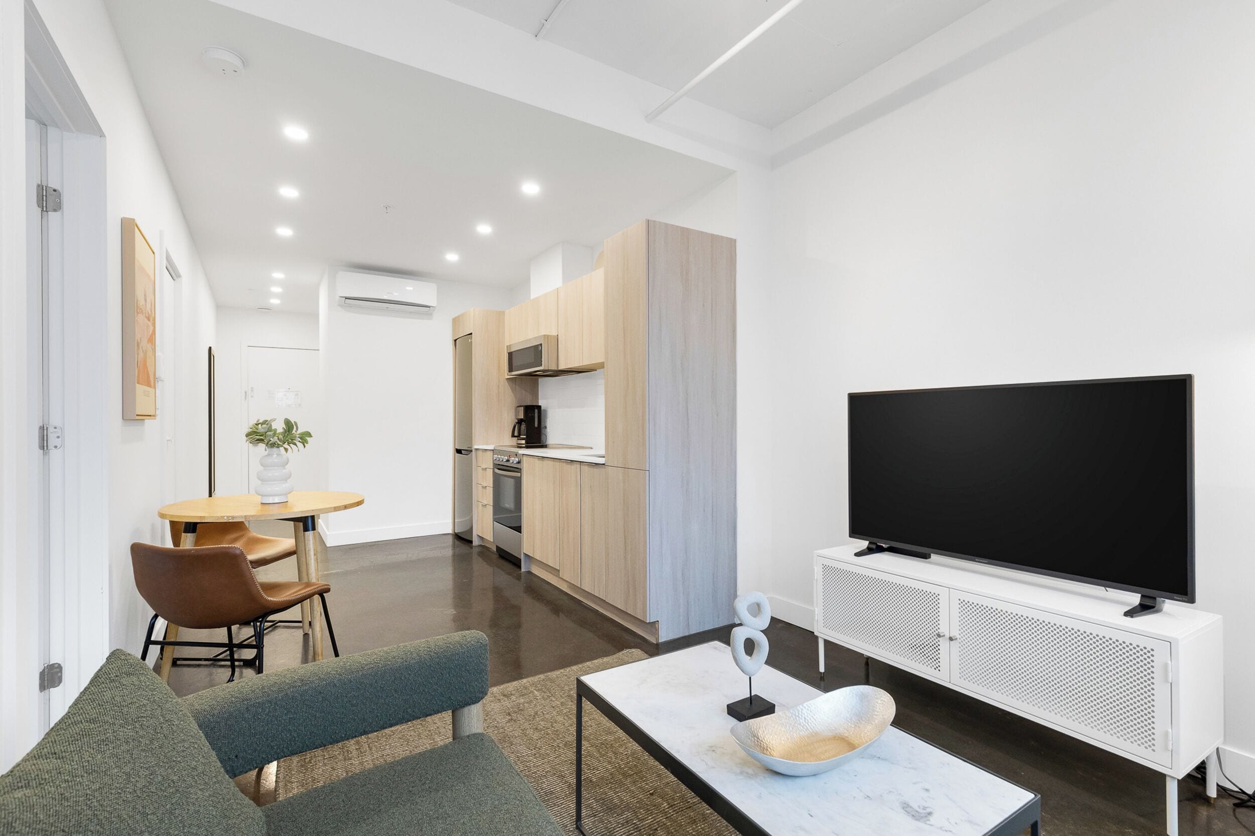 A modern living room with a flat-screen TV, a sofa, a coffee table, and a dining area with a table and chairs.