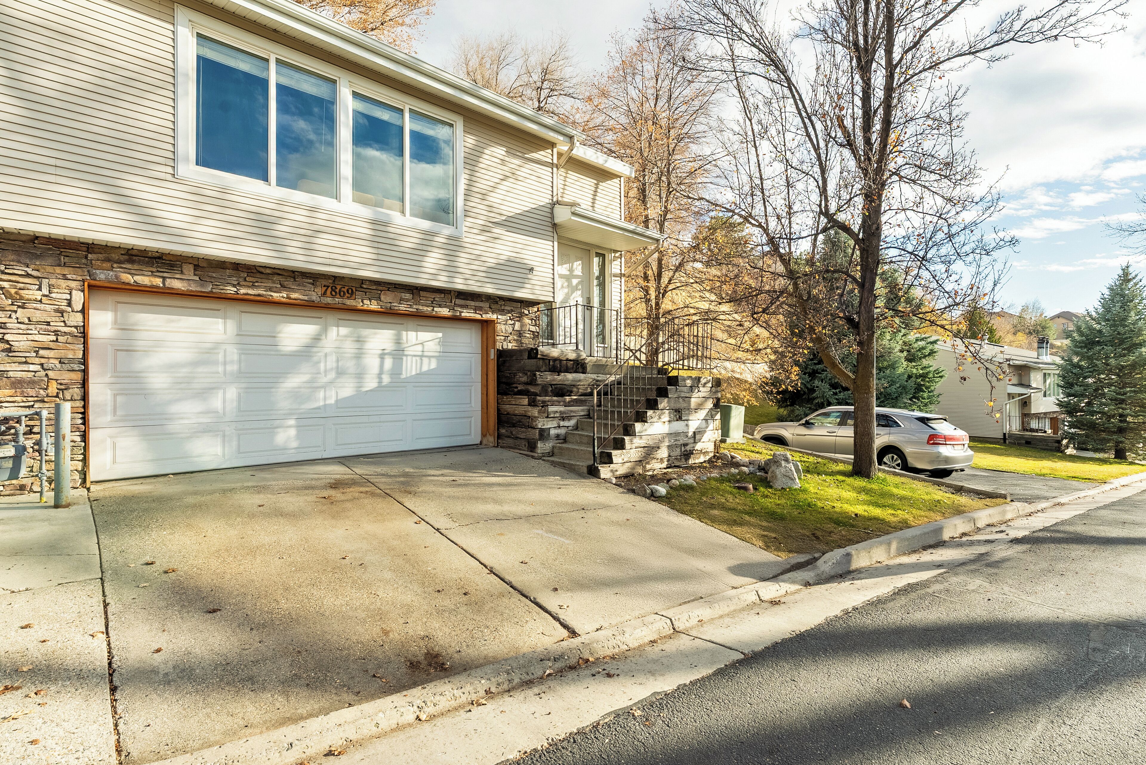 A residential house with a garage, stone foundation, and a driveway leading to the garage.