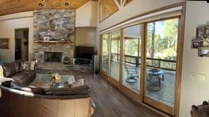 A spacious living room with a stone fireplace, leather furniture, and large windows overlooking a deck.