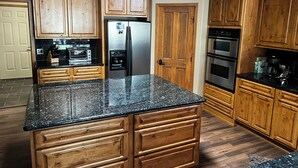 A kitchen with wooden cabinets, a stainless steel refrigerator, a built-in oven, and a granite countertop.
