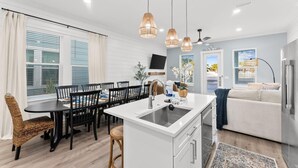 Et moderne køkken med en central ø, spiseplads med stole og en opholdsstue med sofa.