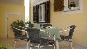 A dining area with four wicker chairs and a table covered with a green tablecloth. There are two windows with wooden shutters, one of which has a potted plant on the windowsill. - 1 bedroom cozy apartment in Labin (Labin)