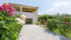 A building with a paved entrance, surrounded by lush greenery and flowering plants. - 1 bedroom cozy apartment in Labin (Labin)