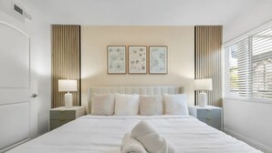 A hotel room with a large bed, two bedside tables, a headboard, and three framed pictures on the wall. - Cozy King Suite Near Bayshore | Pool & Gym (Tampa)