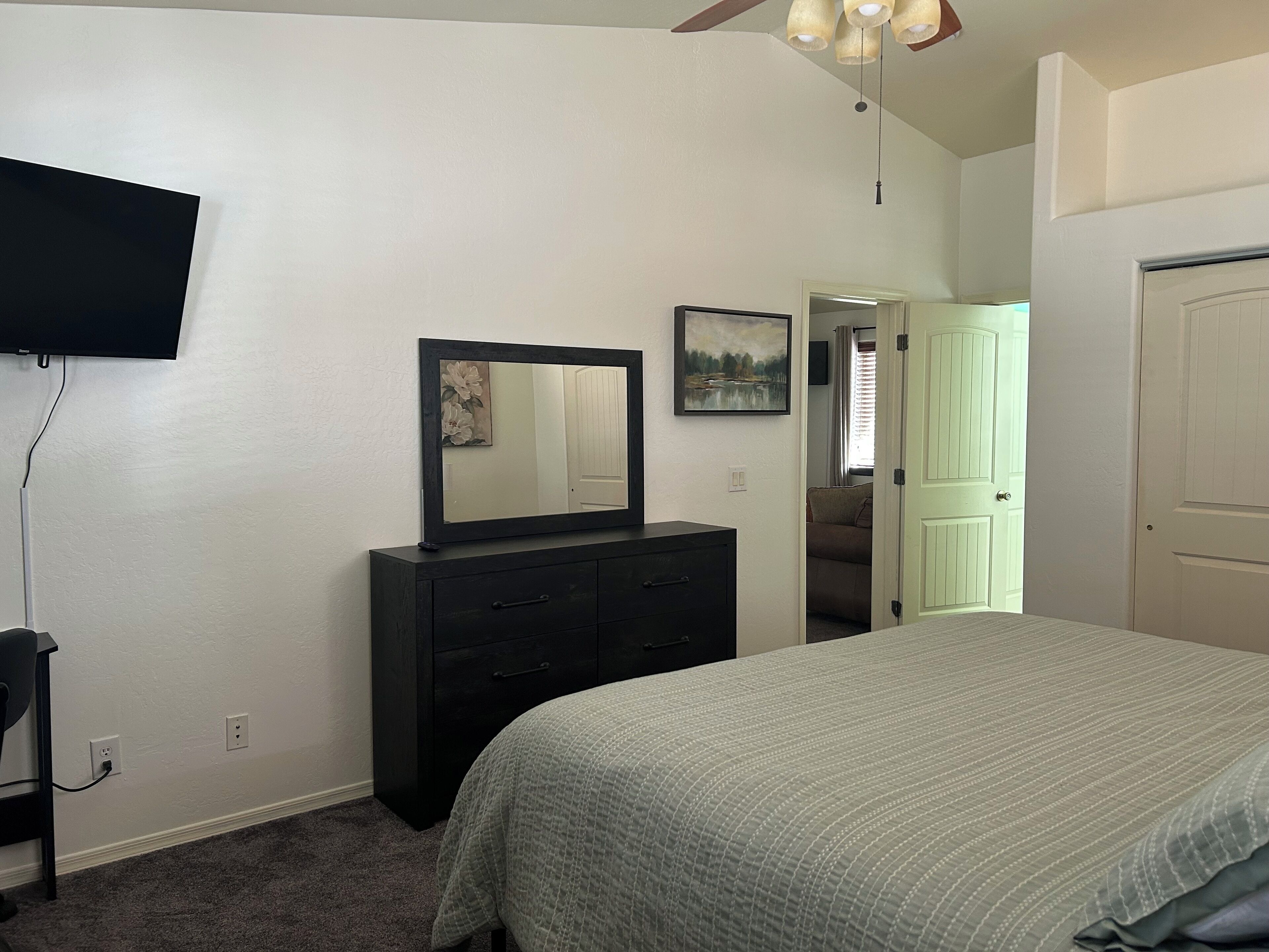 Un dormitorio con cama, cómoda, televisión y una puerta que da a otra habitación.