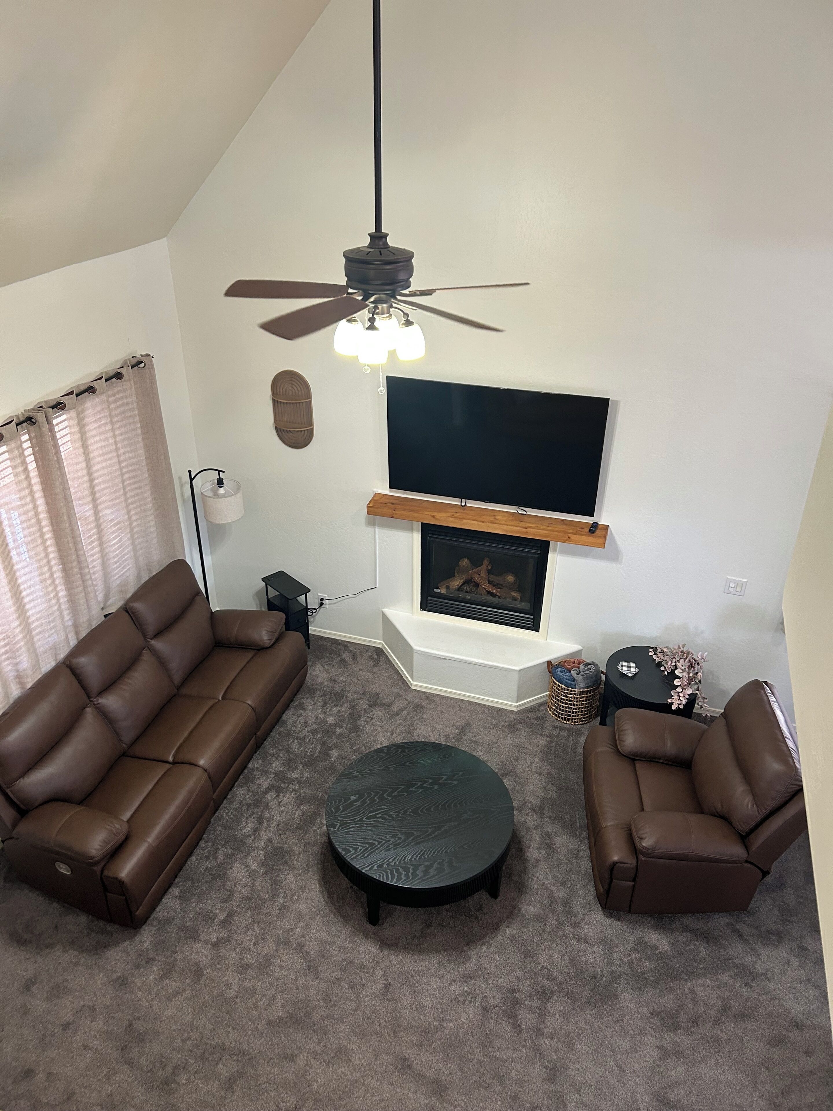 Un salon avec une cheminée, deux canapés, une table basse et un ventilateur de plafond.