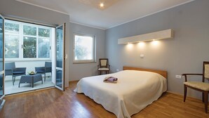 A bedroom with a large bed, a chair, a small table with fruit, and a sliding glass door leading to an outdoor seating area. - 3 bedroom nice apartment in Pula (Pula)