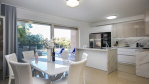 A modern kitchen with a central island, white cabinetry, and a dining area with a glass table and white chairs. - Stunning apartment in Pula (Pula)