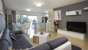 A modern living room with a grey sofa, a flat-screen TV, and a kitchen in the background. - Stunning apartment in Pula (Pula)