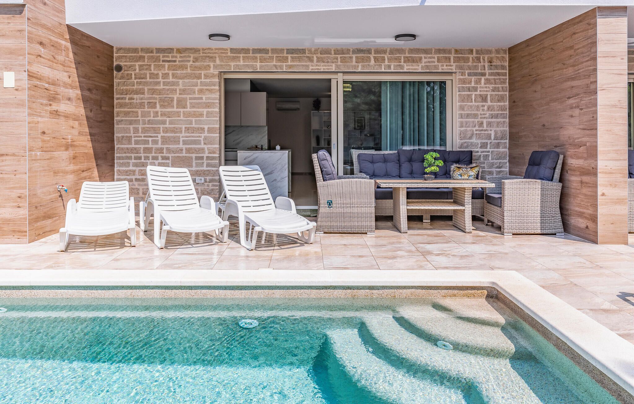 Un área junto a la piscina con sillas de descanso, una mesa y un sofá.