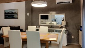 Uma sala de jantar com uma mesa de madeira e cadeiras brancas, um espelho grande acima da mesa e um quadro na parede.