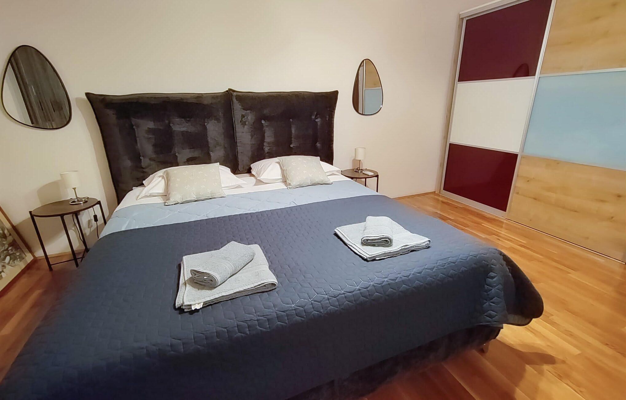 Ein ordentlich gemachtes Bett mit einer dunkelblauen Decke, zwei Kissen und gefalteten Handtüchern.