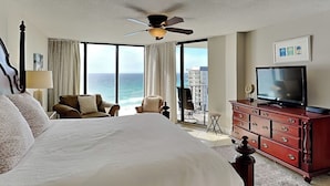 Een hotelkamer met een groot bed, een televisie, een dressoir en een balkon met uitzicht op de oceaan.