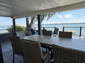 Een overdekt terras met rieten meubilair en uitzicht op het water.