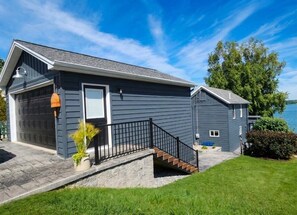 Een twee verdiepingen tellend huis met een garage, een veranda met een zwarte balustrade, en een kleine trap die naar de ingang leidt.
