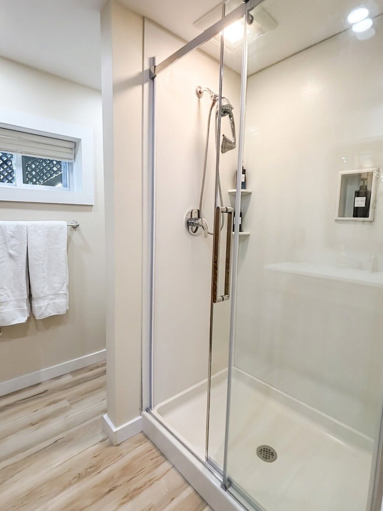 A modern bathroom with a glass-enclosed shower, a white towel rack, and a small shelf with toiletries.