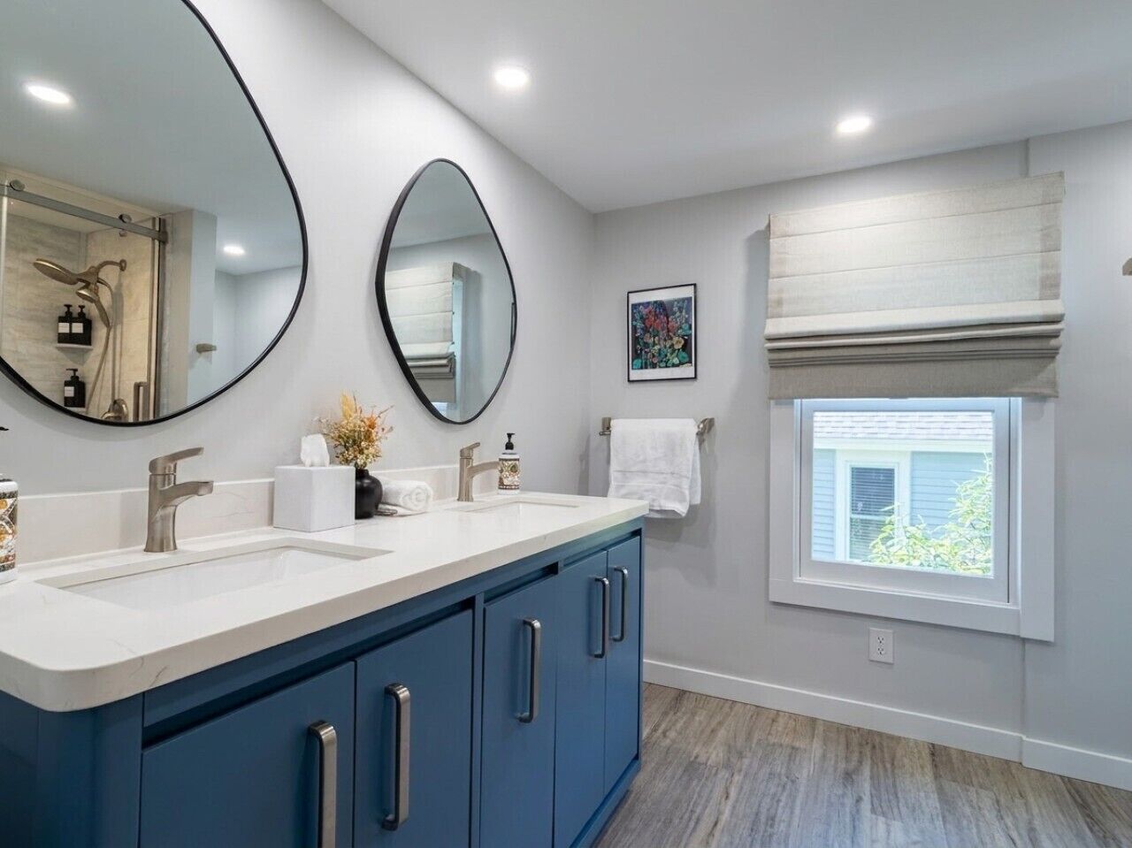 A bathroom with a double vanity, a large mirror, a window with blinds, and a towel rack.
