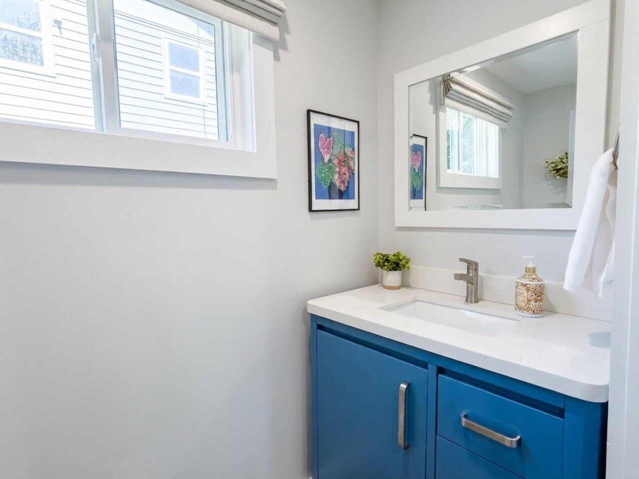Un baño con lavamanos blanco, armarios azules, un espejo y una ventana.