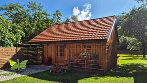 Une cabane en bois avec un toit en tuiles, une porte en bois et un petit porche agrémenté de plantes en pot.
