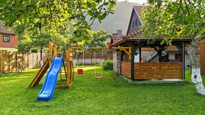 Un jardin avec une balançoire en bois, un toboggan bleu et une petite maison de jeu en bois.