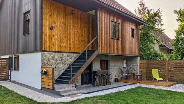 Une maison moderne à deux étages, dotée d’une façade en pierre, d’un revêtement extérieur en bois et d’un petit espace extérieur aménagé pour s’asseoir.