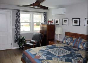 Ein Schlafzimmer mit einem Bett, einem Sessel, einer Lampe, einer Pflanze und einem Fenster mit Vorhängen.