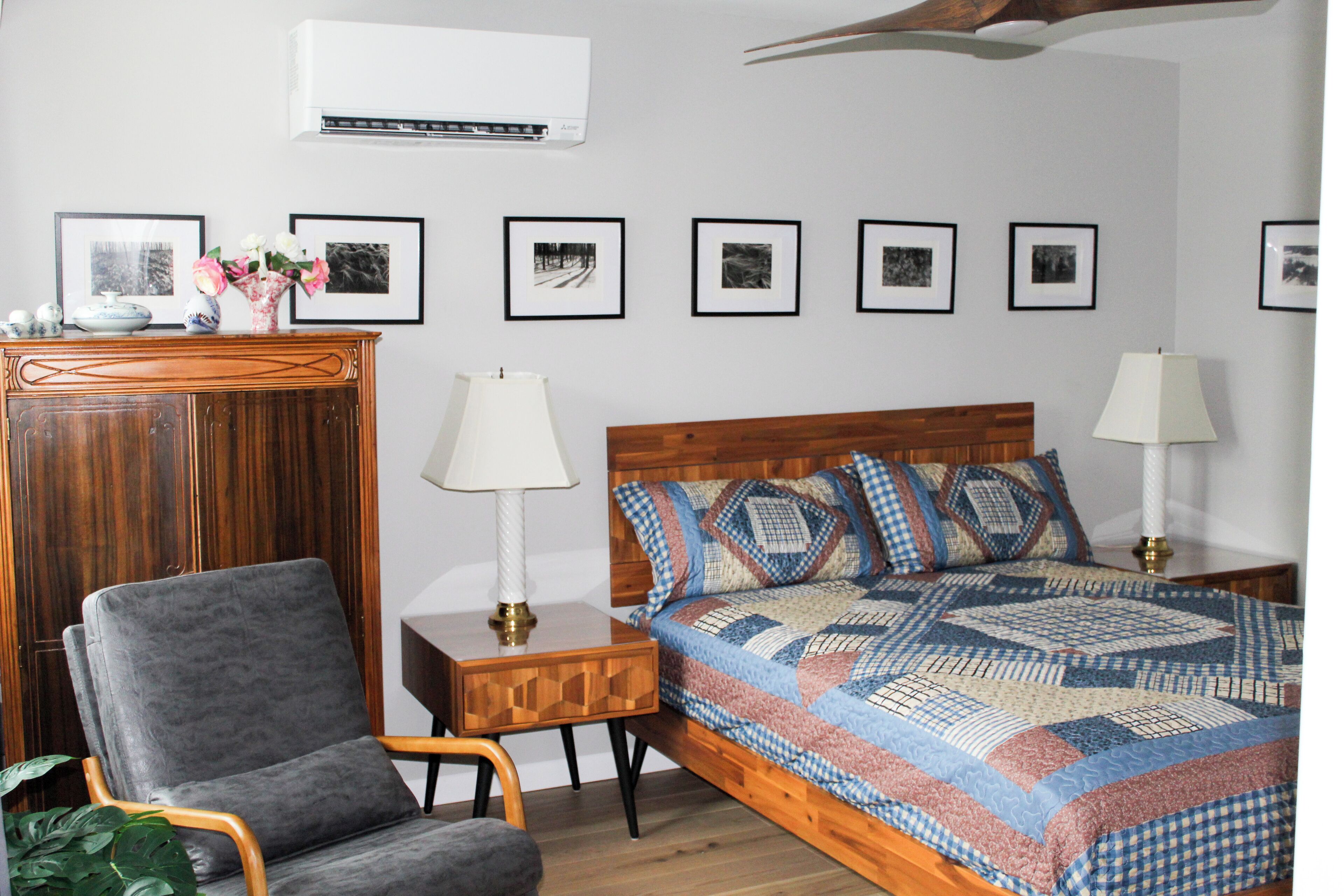 A bedroom with a wooden headboard, a grey armchair, a bedside table with a lamp, and a quilted bedspread.