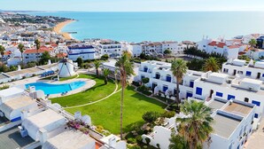 Un hotel costero con piscina, edificios blancos y vista a la playa y al mar.